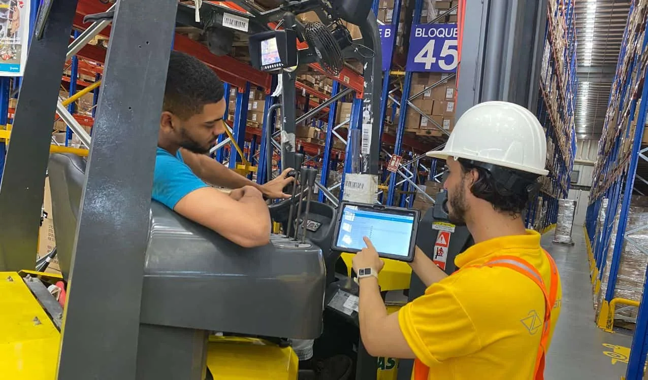 Operario de almacén revisando pedidos en una tableta junto a una carretilla